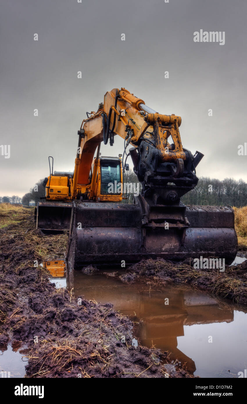 Yellow digger on a muddy site under dark clouds Stock Photo