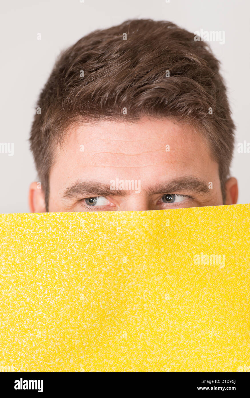 Face of adult male peeking and looking sideways hidden behind sandpaper Stock Photo