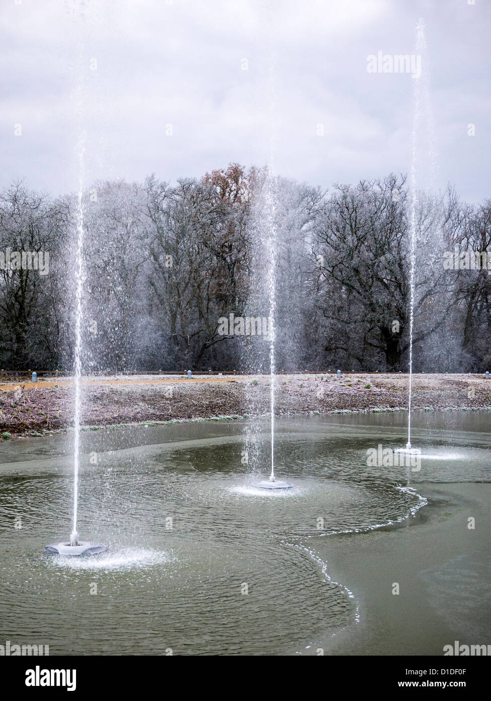 Fountains at Chobham Service Station on the M25 gushing jets of water cascading back down onto a frozen pond Stock Photo