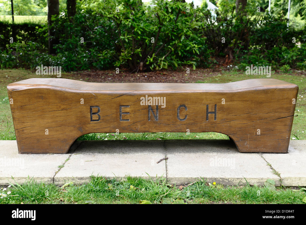 An empty wooden park bench with the word bench carved on the front in
