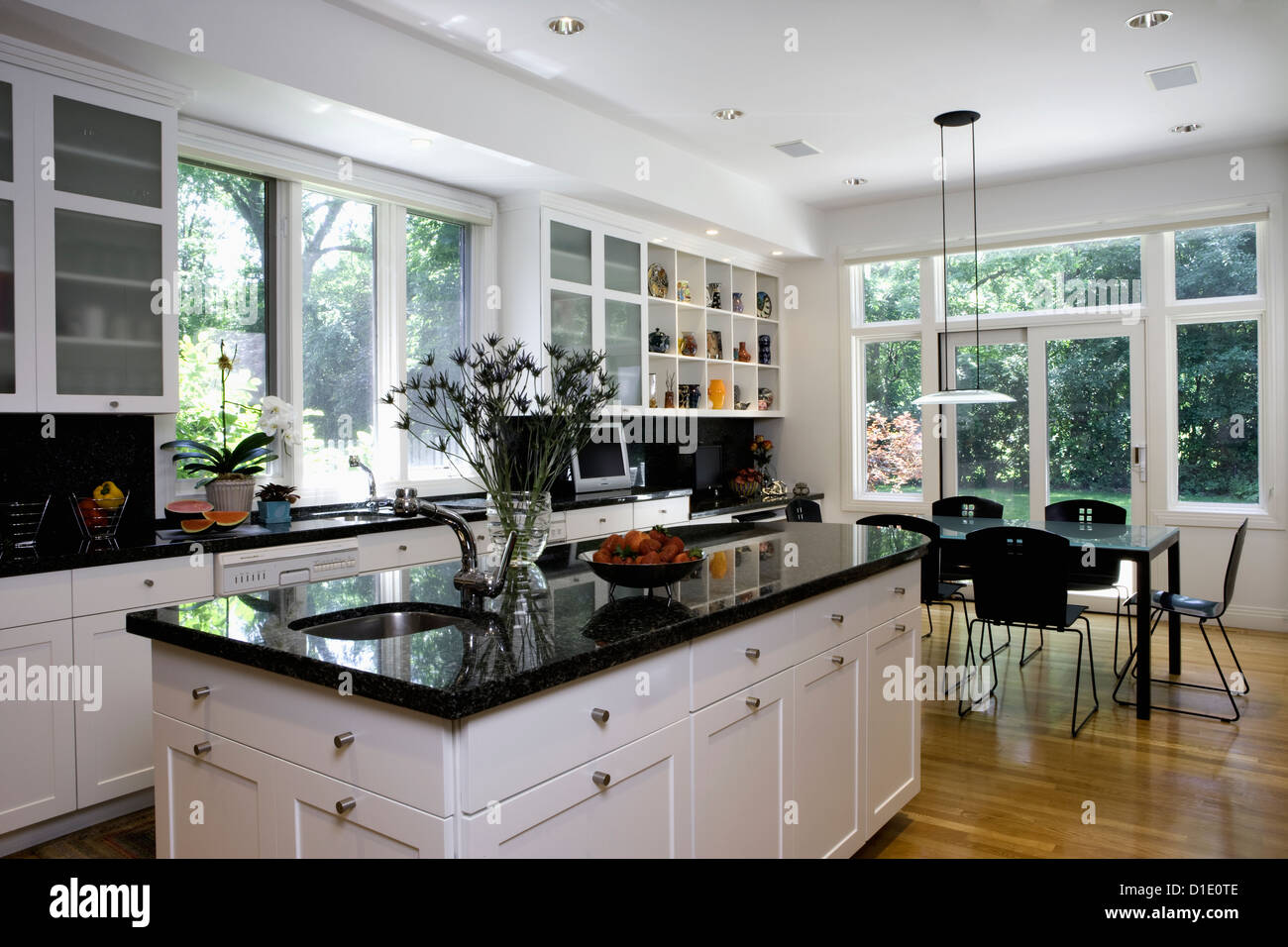 KITCHENS island in foreground dark granite eating area beyond with pendant style light fixture collection display above desk Stock Photo