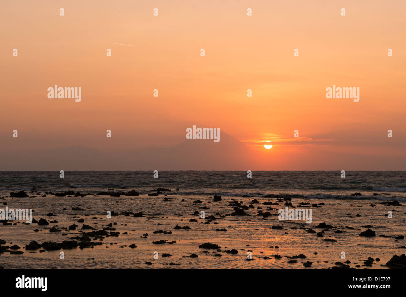 Warm tropical sunset over Agung volcano, the highest mountaint on Bali island, Indonesia with sea and stones on front Stock Photo