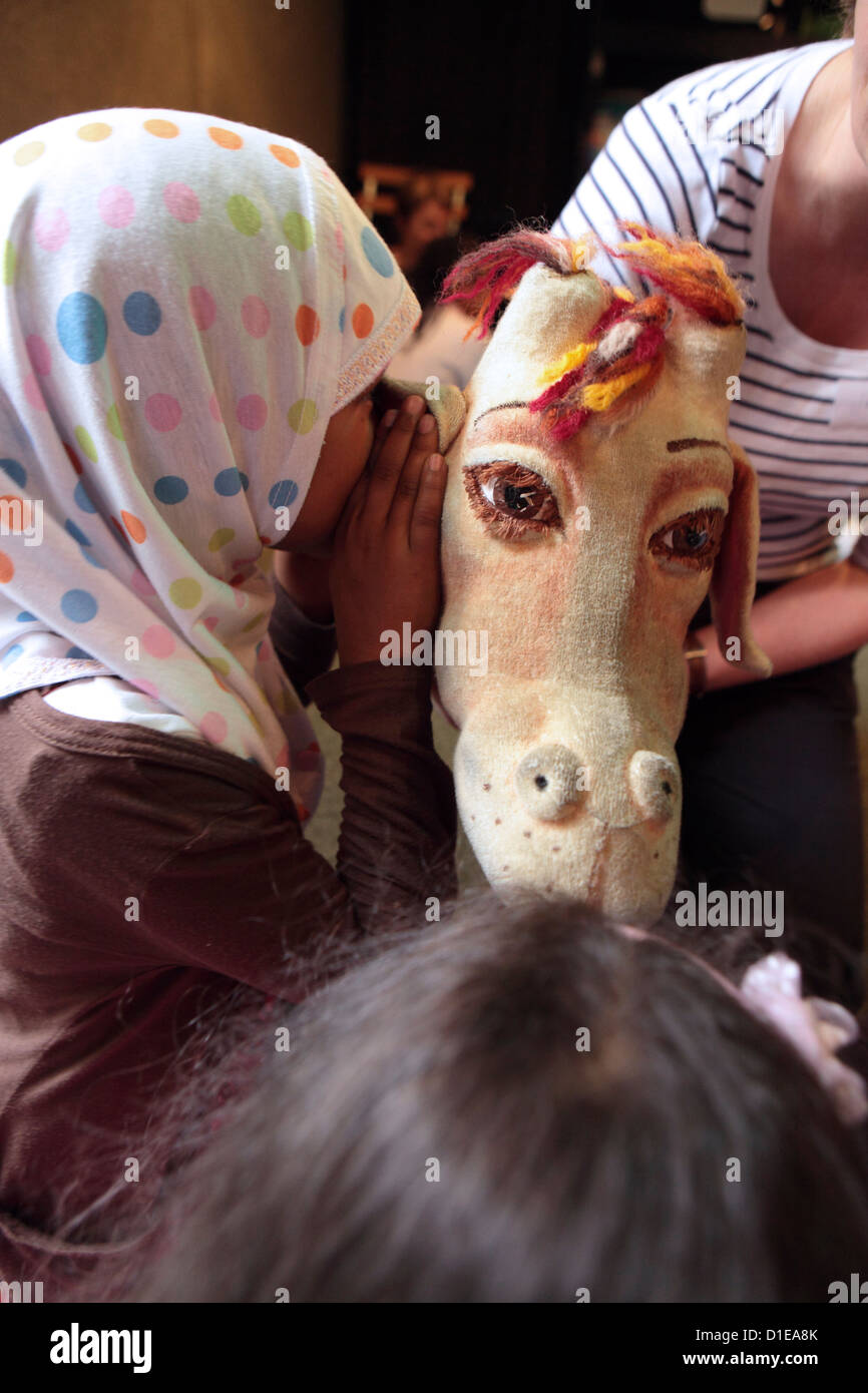 Child girl wearing shawl whispers into ear of puppet horse, London Stock Photo