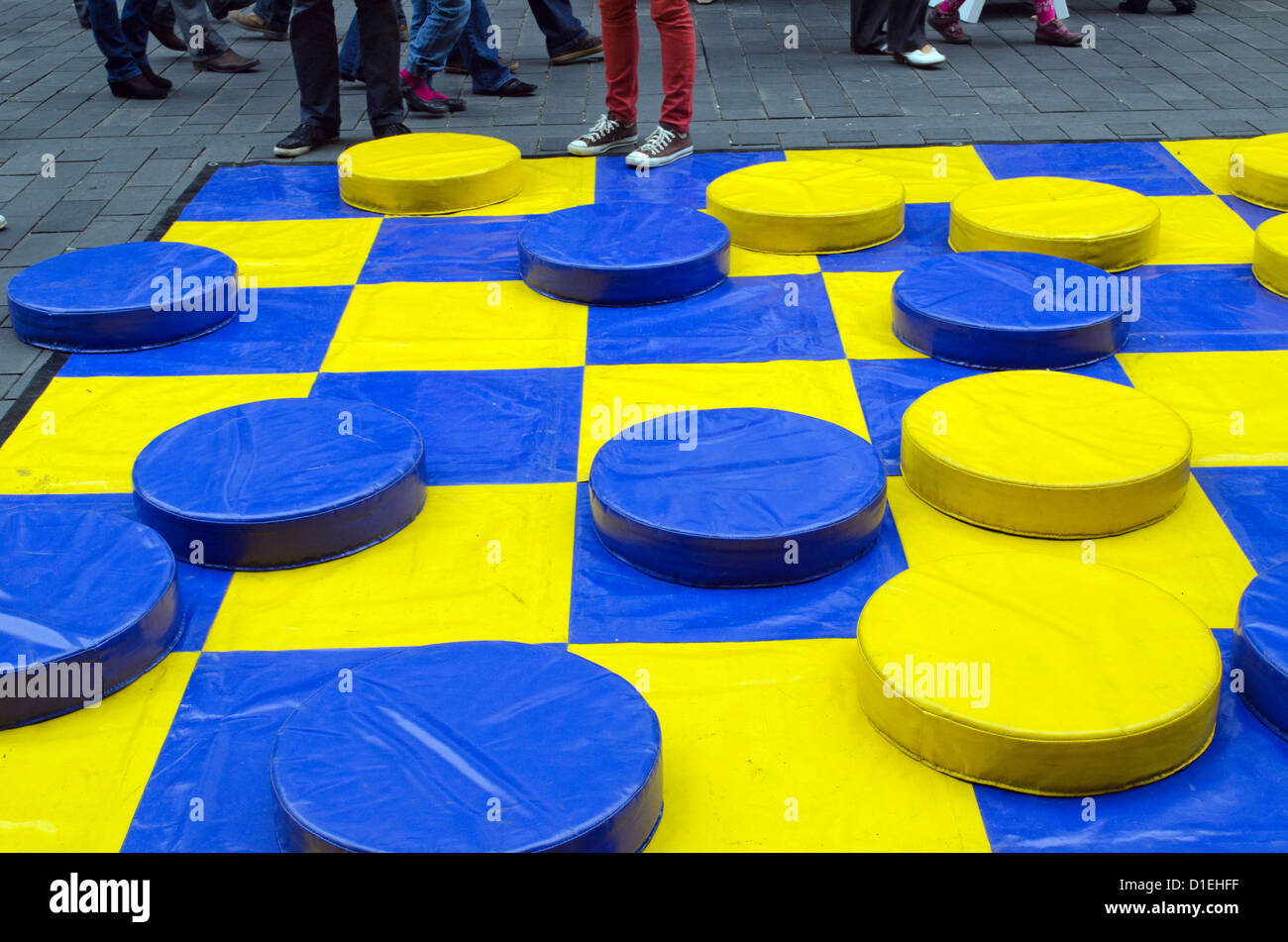 yellow and blue huge checkers figures outdoor and many people legs. people fun entertainment play object in street Stock Photo