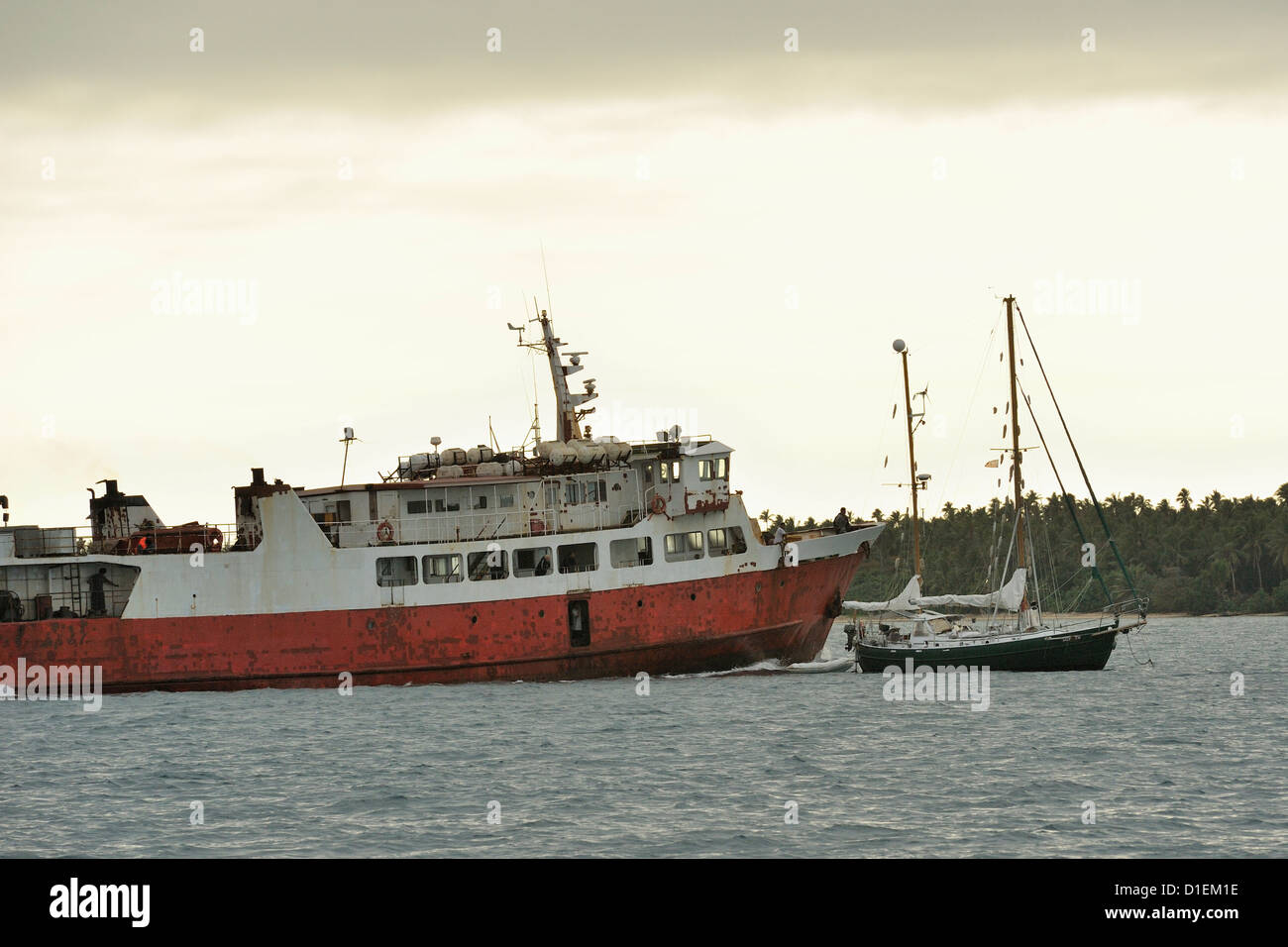 Early morning and an inter island ferry makes a point to a yacht anchored in his approach to Pangai harbour, Tonga Stock Photo
