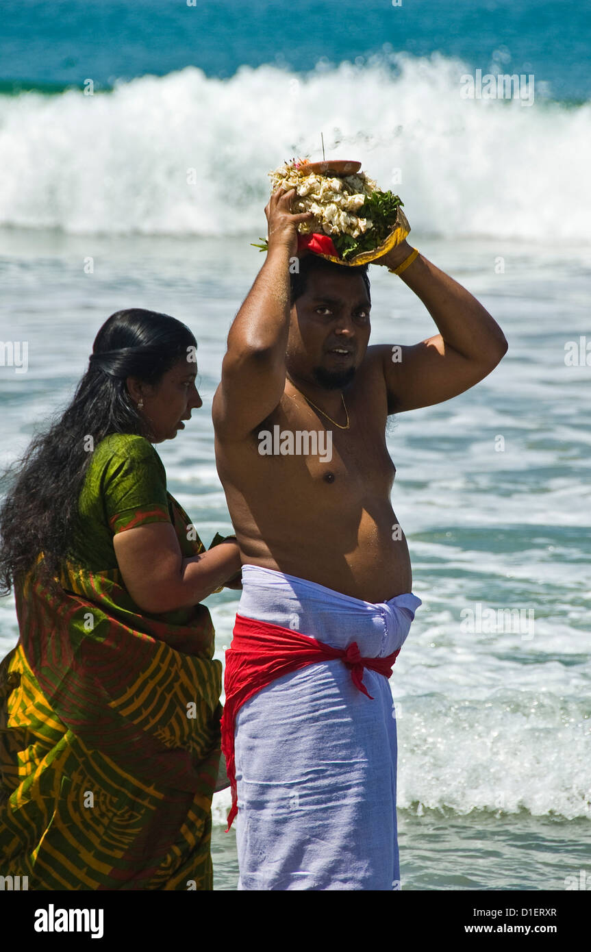 Vertical portrait of an Indian man and woman performing puja (prayers) on the beach at Varkala, Kerala. Stock Photo