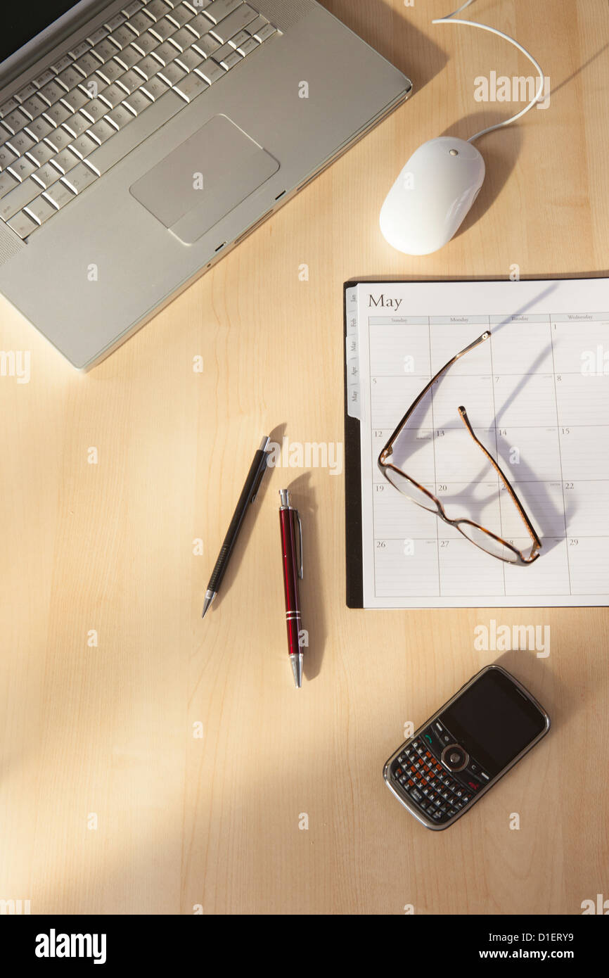 computer and calendar sit on desk top with cell phone, glasses and pens Stock Photo