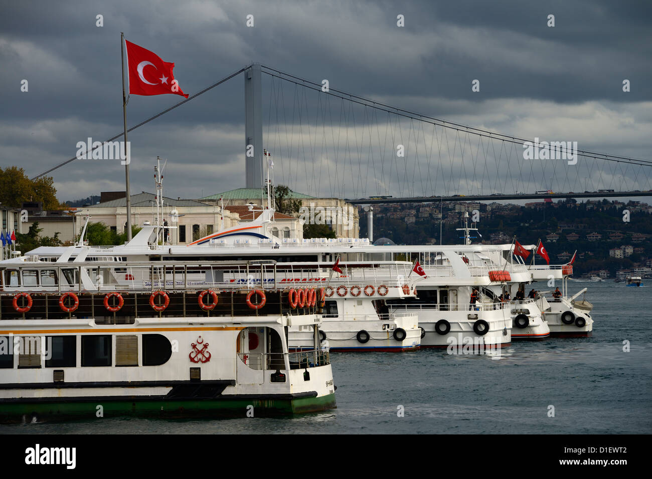 Ferry and tour boats at Besiktas Pier with the First Bosphorus Bridge and Turkish flag Istanbul Turkey Stock Photo