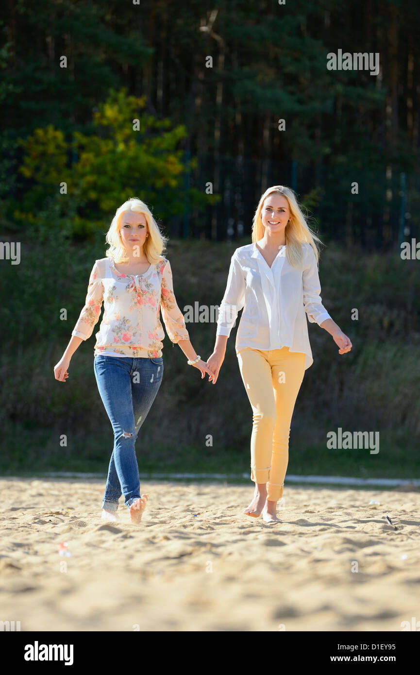 Two happy young blond women walking hand in hand on sandy beach Stock Photo