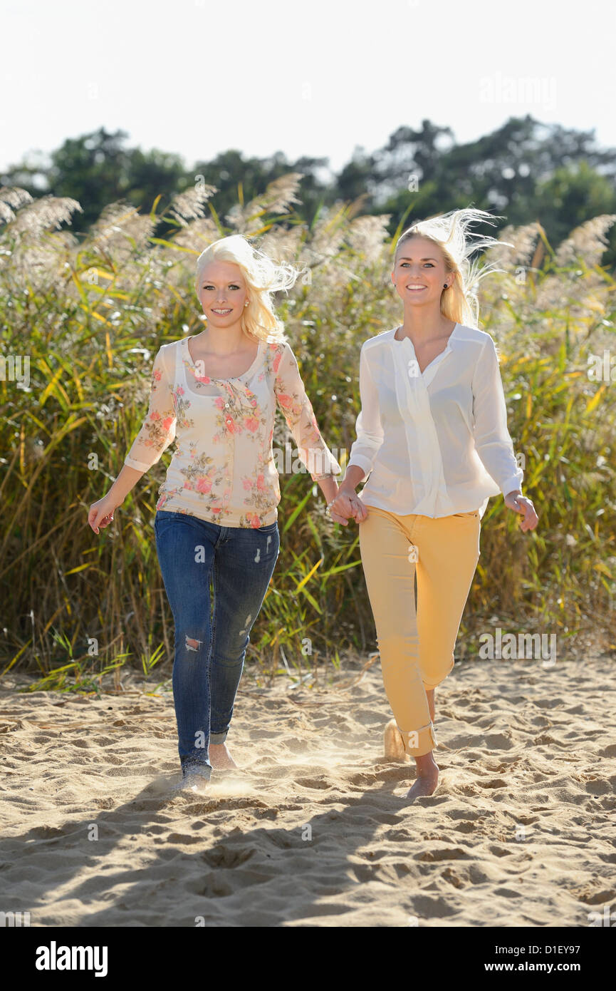 Two happy young blond women walking hand in hand on sandy beach Stock Photo