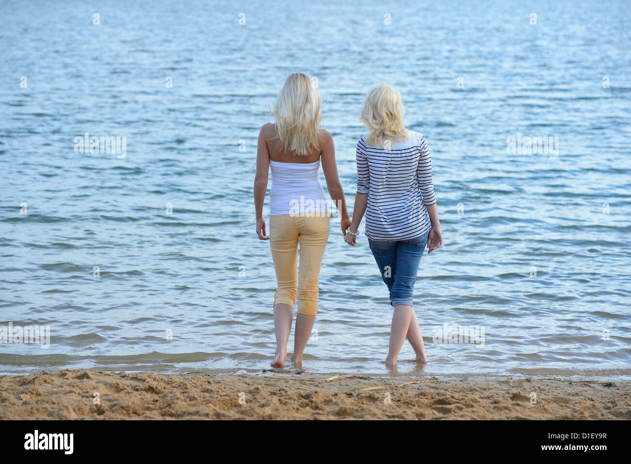 Two young blond women standing hand in hand at bathing lake Stock Photo