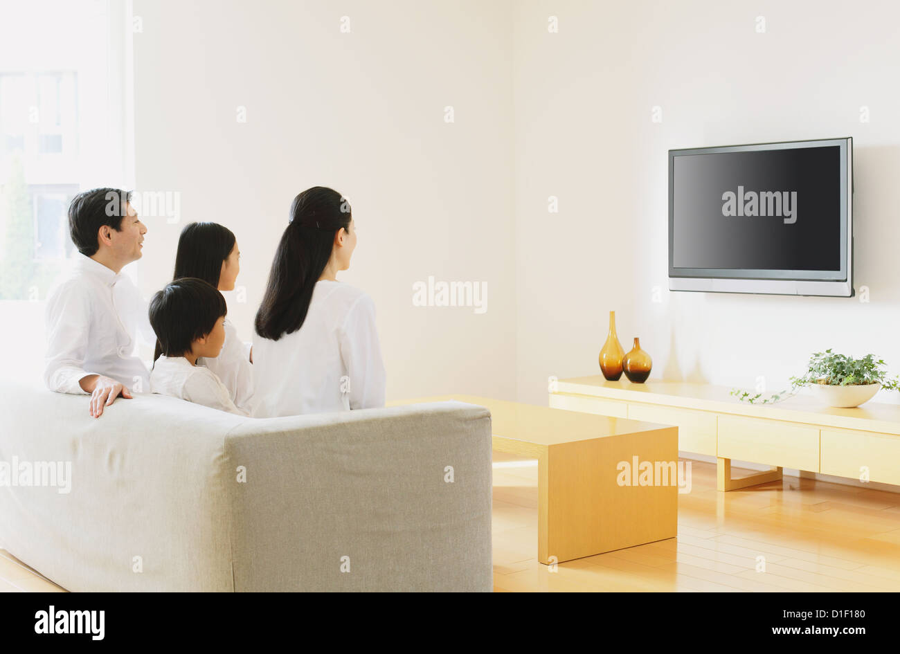 Family of four people watching TV on the sofa in the living room Stock Photo