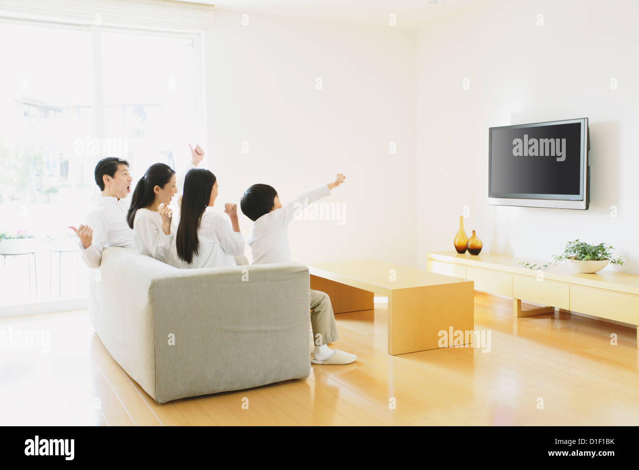 Family of four people watching TV on the sofa in the living room Stock Photo
