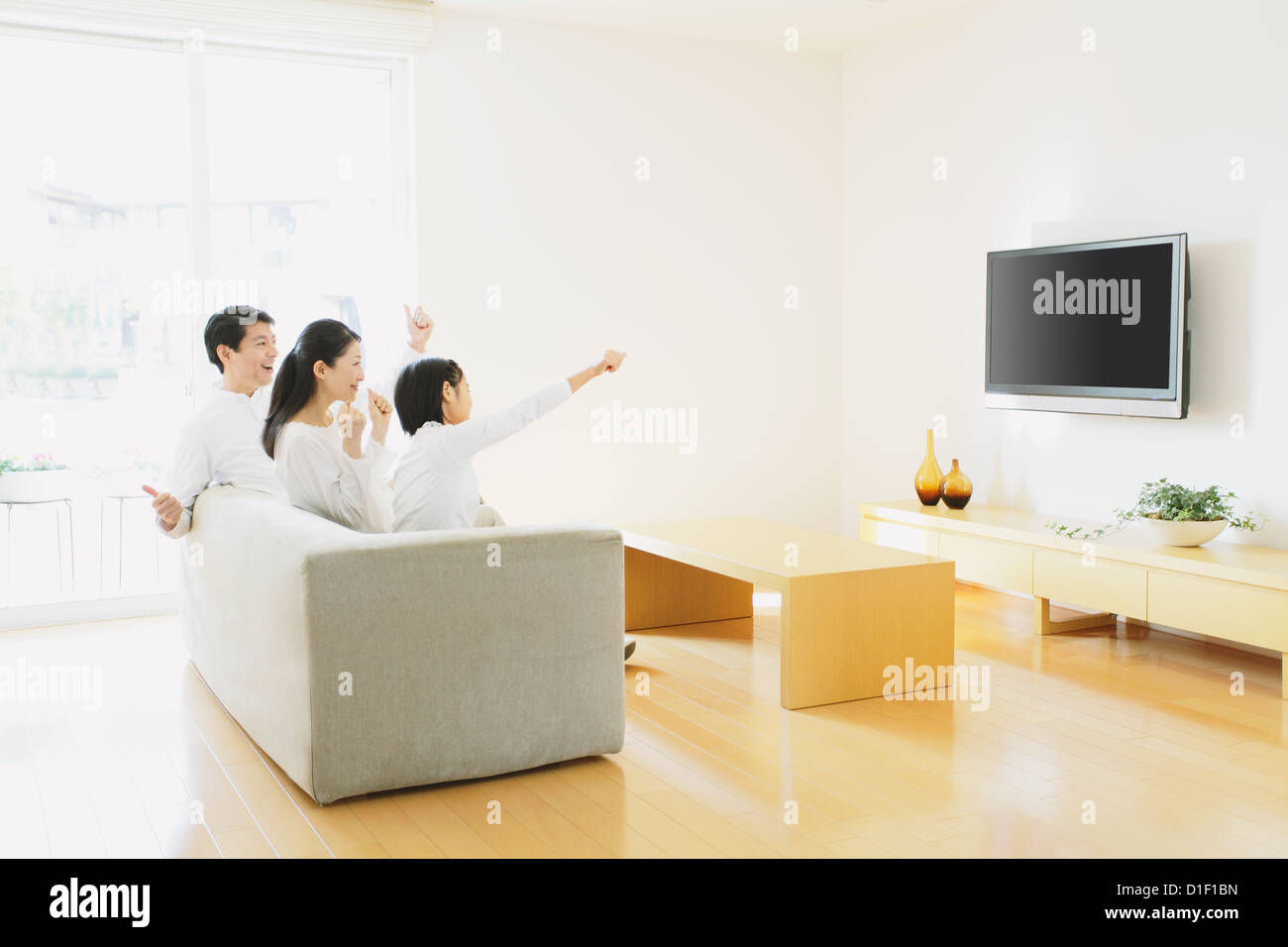 Family of three people watching TV on the sofa in the living room Stock Photo