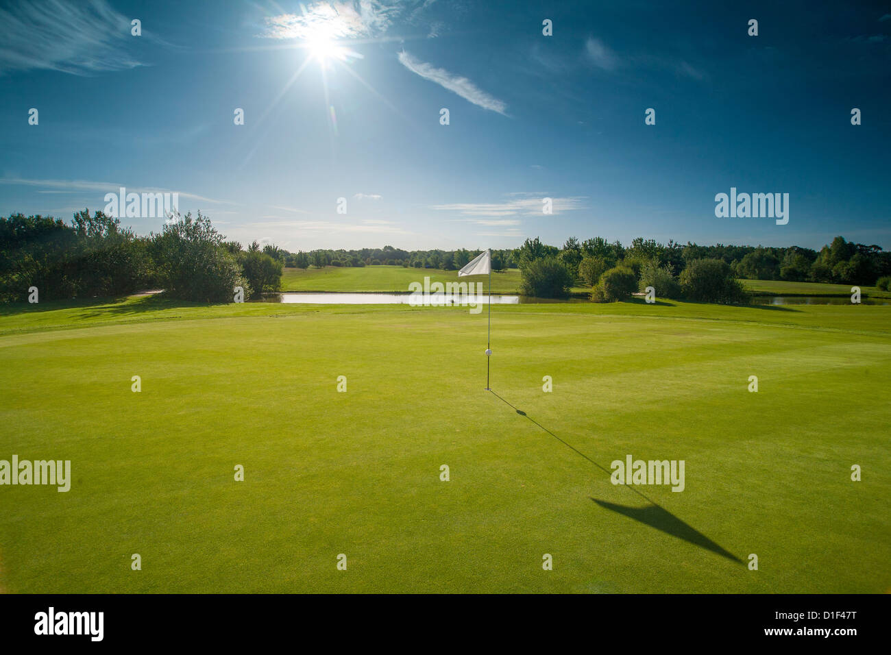 Midday sun over golf course, flag with long shadow. Stock Photo