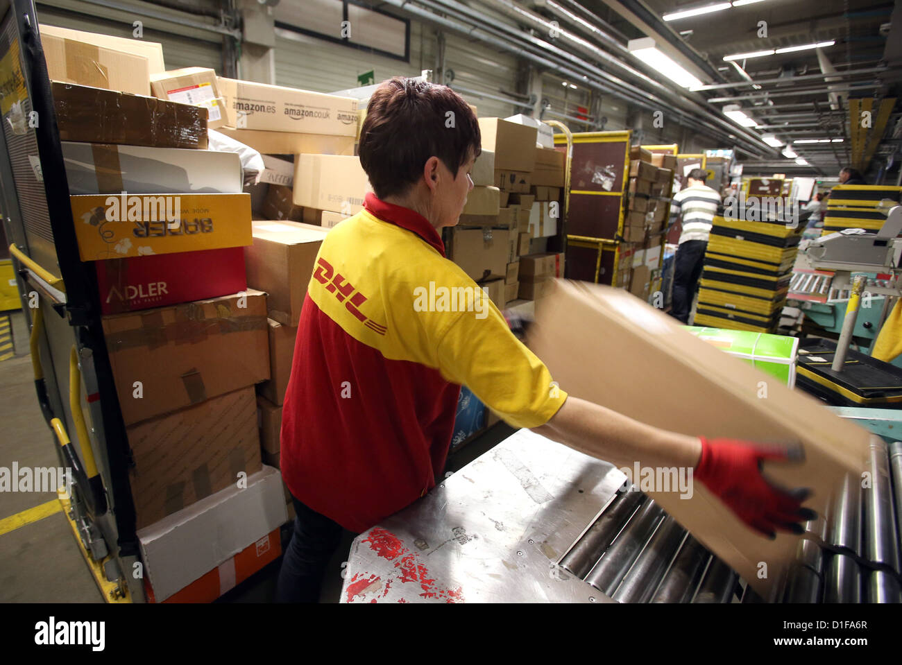 Karin Simon puts packages on the conveyor belt at the parcel sorting center of Deutsche Post DHL in Neustrelitz, Germany, 17 December 2012. Up to 20,000 parcels are sorted in an hour. Since November, the traffic doubled, and six million packages are sorted in total. Nationwide, Deutsche Post DHL expects a record in the number of packages delivered in the Christmas period. Photo: Bernd Wüstneck Stock Photo