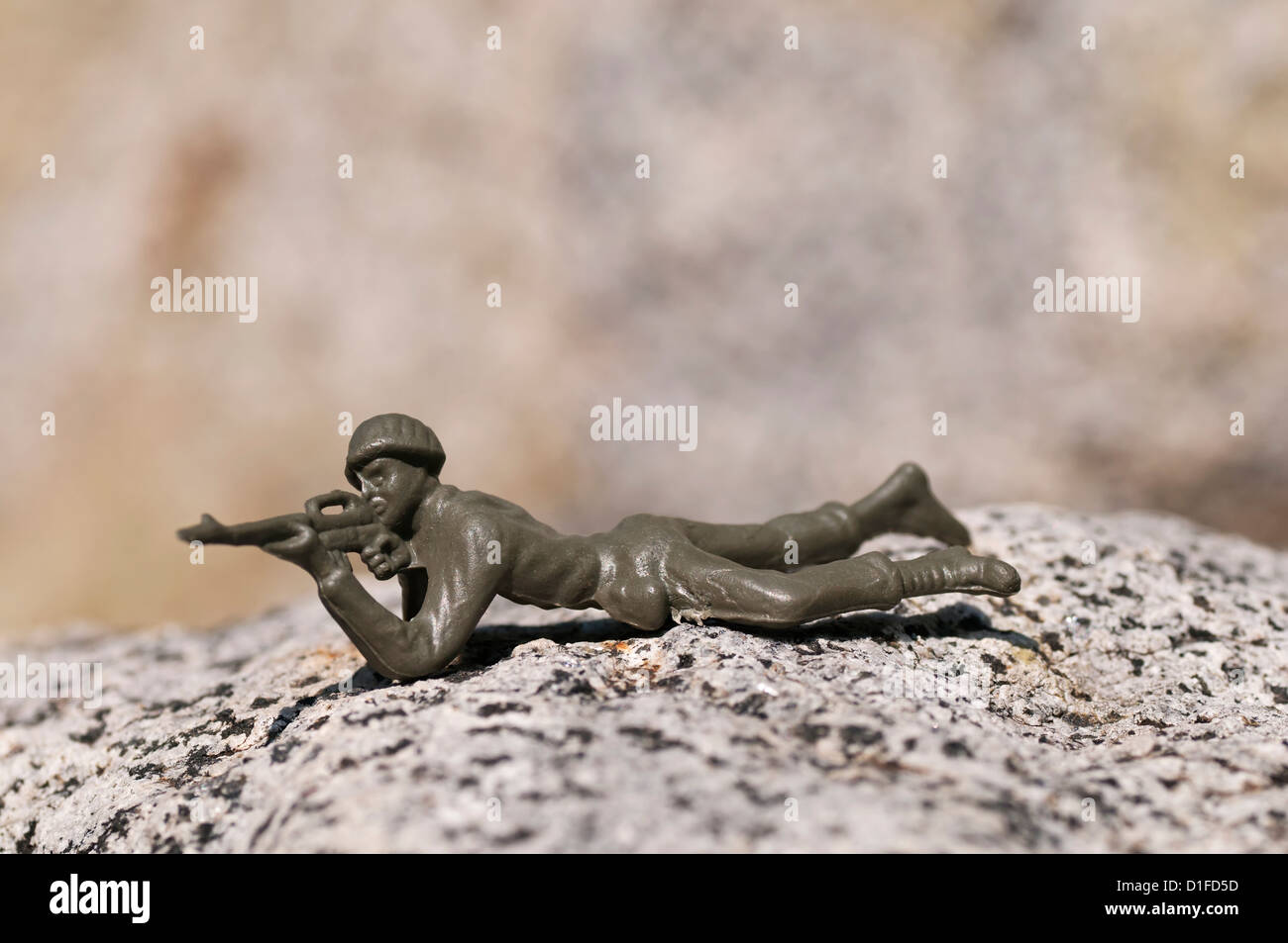 A green plastic toy soldier lies prone outdoors while aiming his rifle. Stock Photo