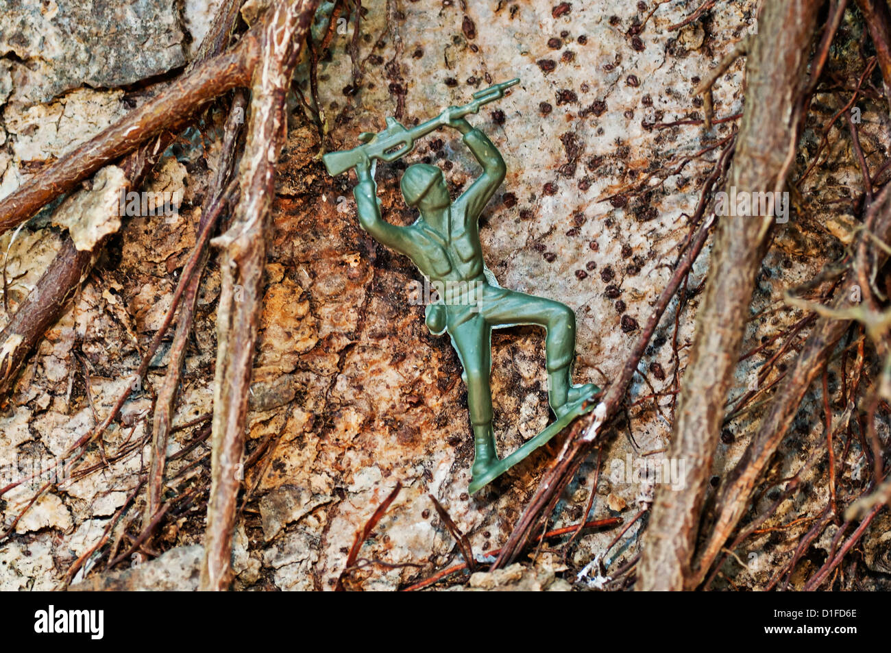 A green plastic toy soldier holds his rifle overhead while climbing in a difficult location outdoors. Stock Photo