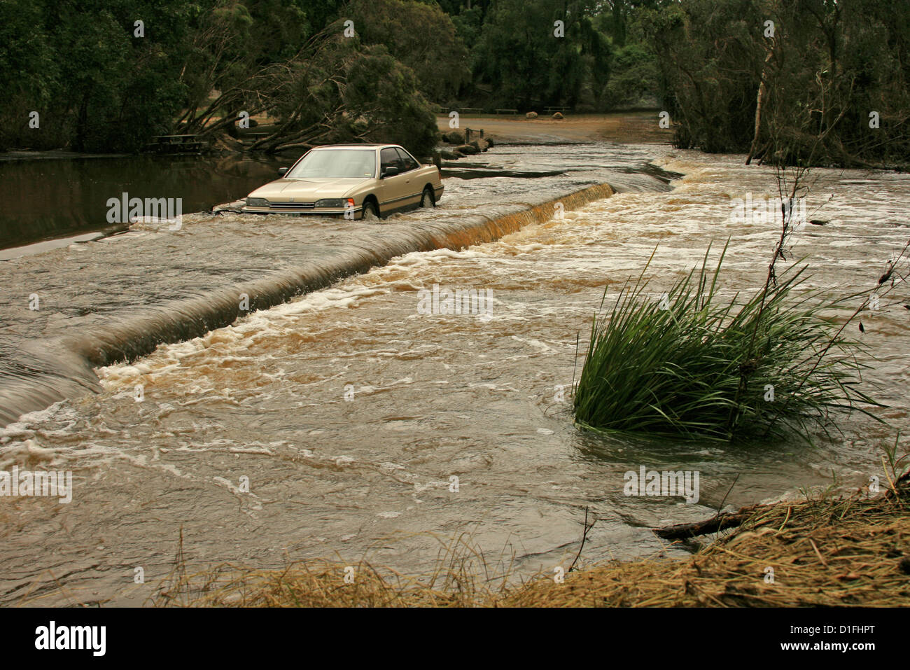 Car been driven through dangerously deep and fast flowing floodwaters of rivercrossing a road in Australia Stock Photo