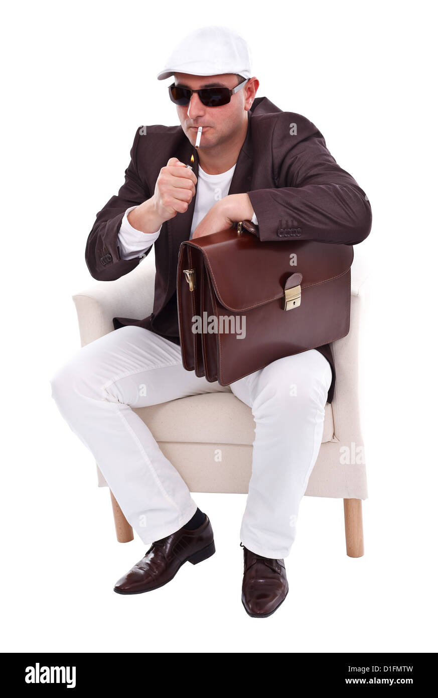 Man sitting in armchair lighting his cigarette, studio shot Stock Photo