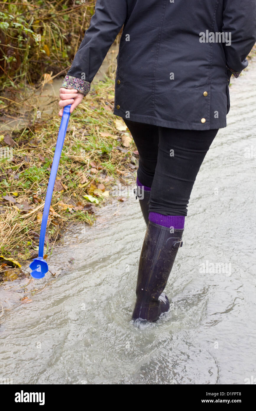 Woman wearing a Barbour and Hunter wellies carrying a ball throwing stick for a dog Stock Photo