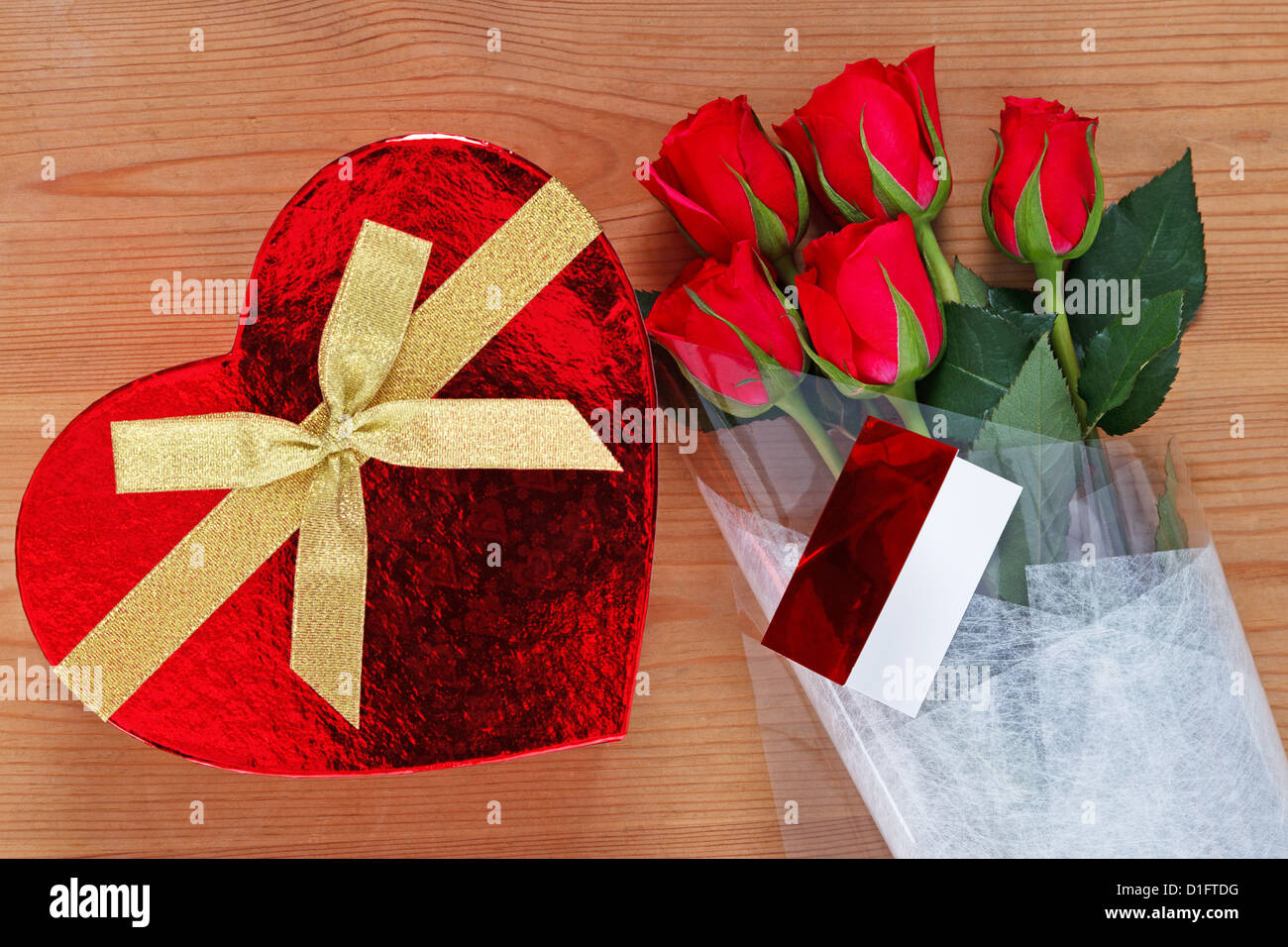 Chocolates in a heart shaped box and a bunch of red roses with card on an old wooden table. Stock Photo