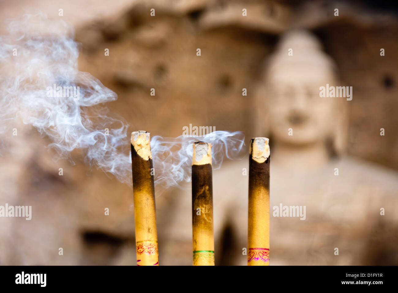Three burning incense in front of a huge buddha statue. The focus is on