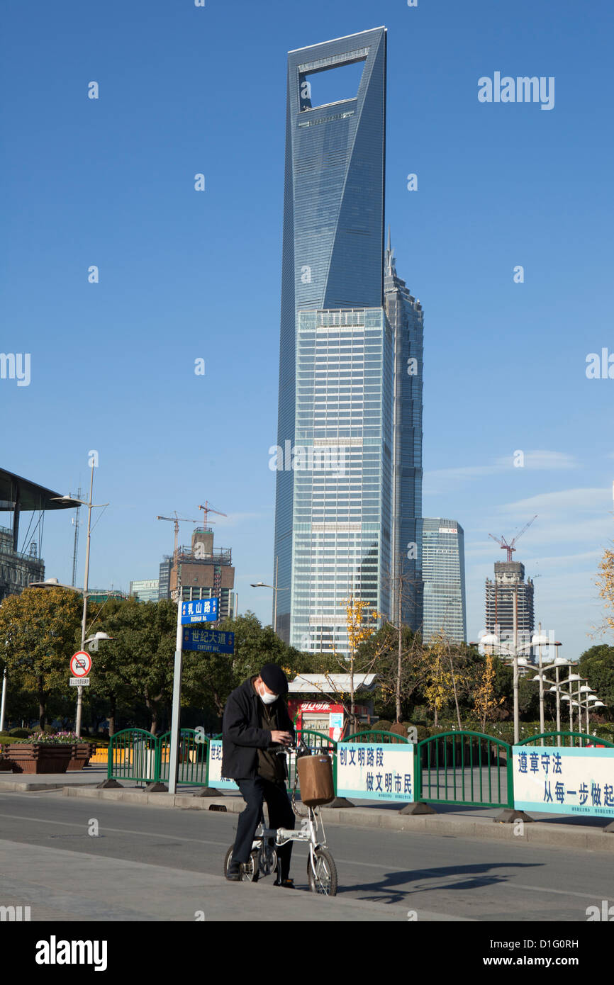Man checking his mobile phone on his bicycle, with the 'Bottle Opener' in the background. Pudong,Shanghai, China, 2009. Stock Photo