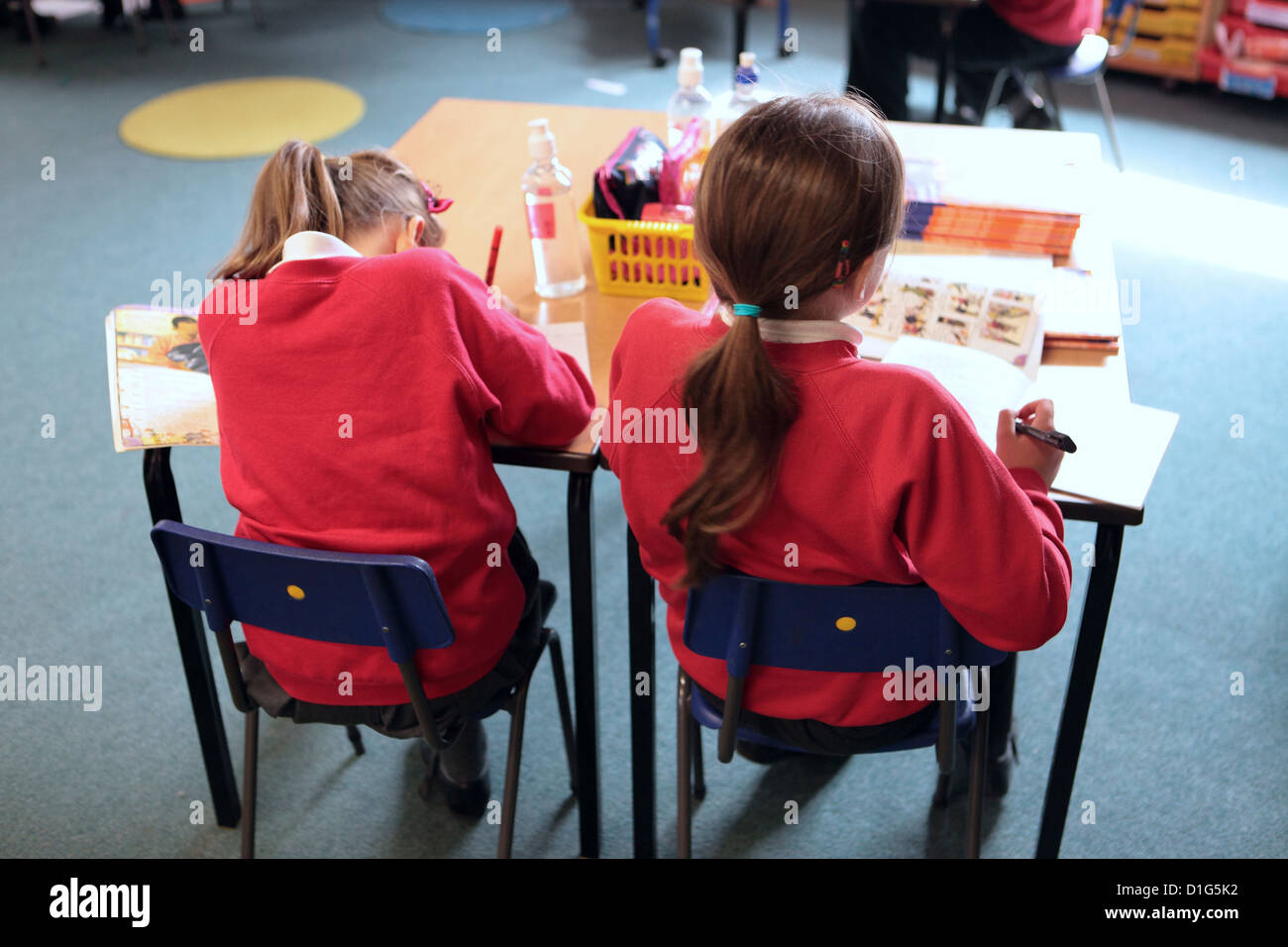 Two primary school girls sat sitting at desk table working, rear view, Primary School, UK Stock Photo