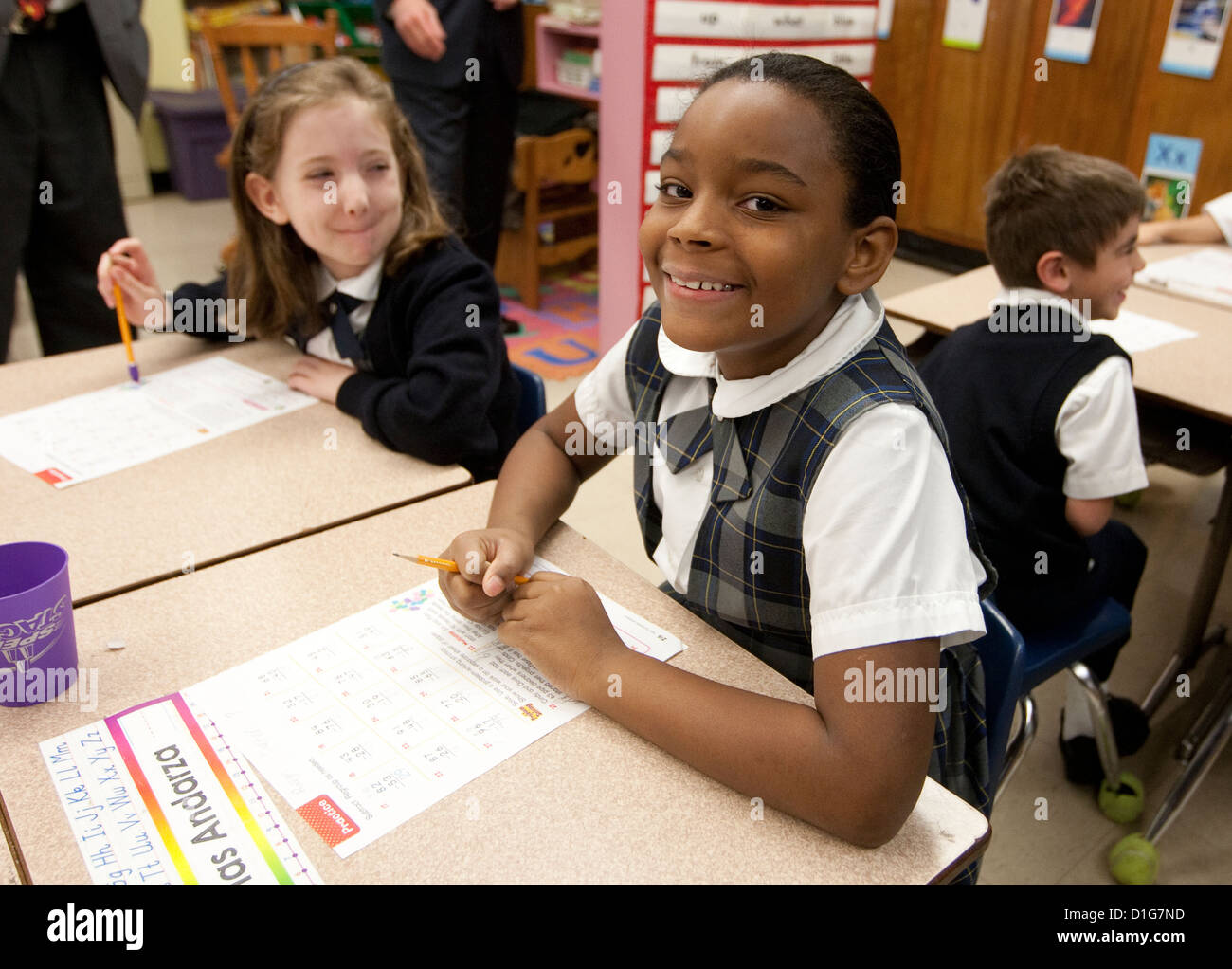 Second grade elementary  children girls Anglo and African-American wearing uniforms complete school work at Catholic school Stock Photo