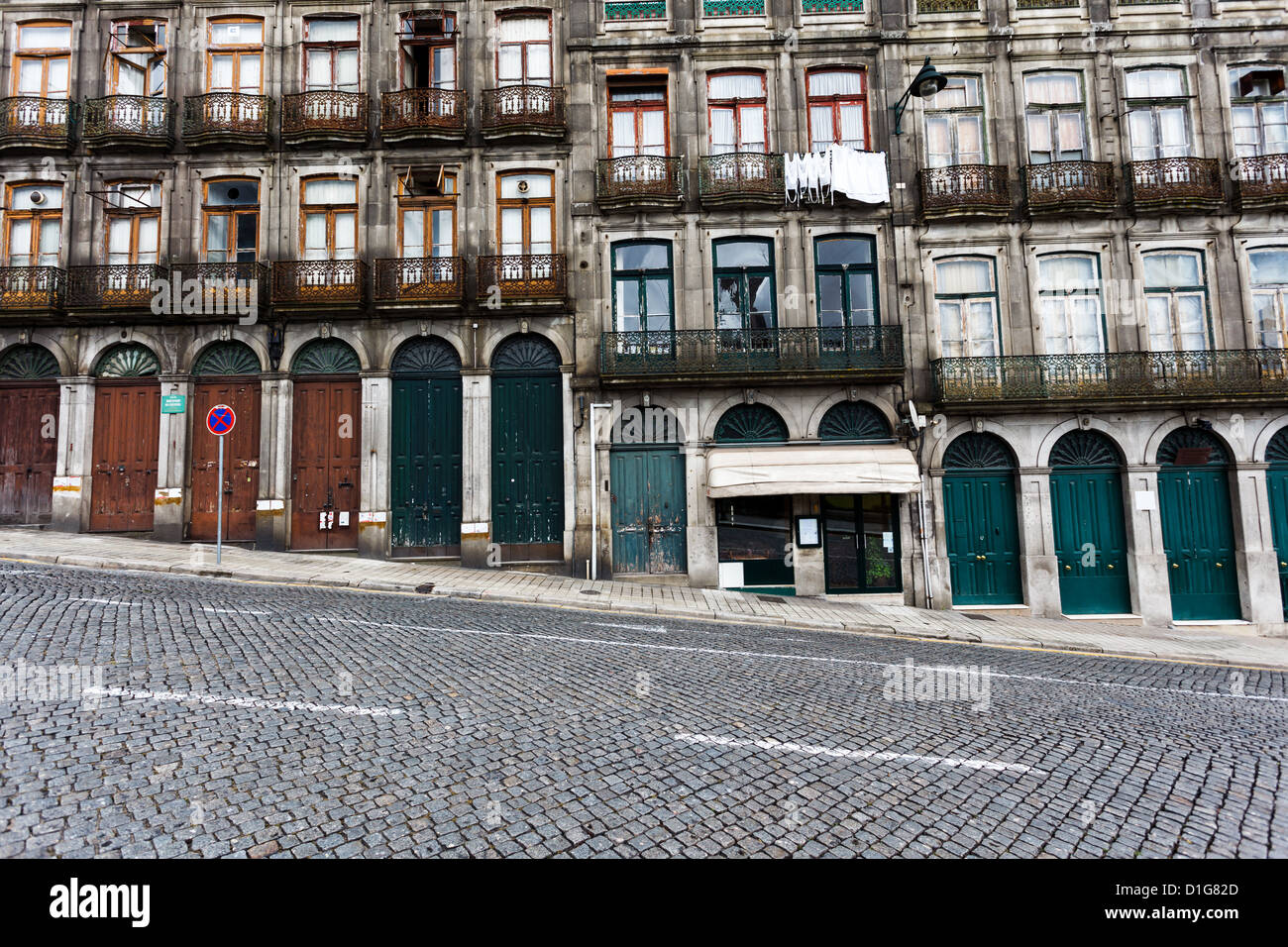 Facade of the lower stories of an apartment house on a steeply sloped cobblestone street in Porto Portgal. Stock Photo
