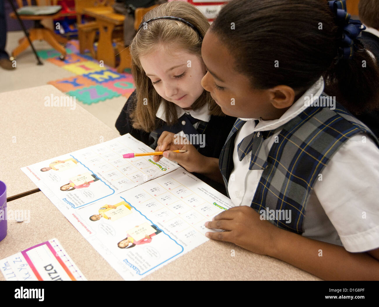 Second grade elementary  children girls Anglo and African-American wearing uniforms complete school work at Catholic school Stock Photo