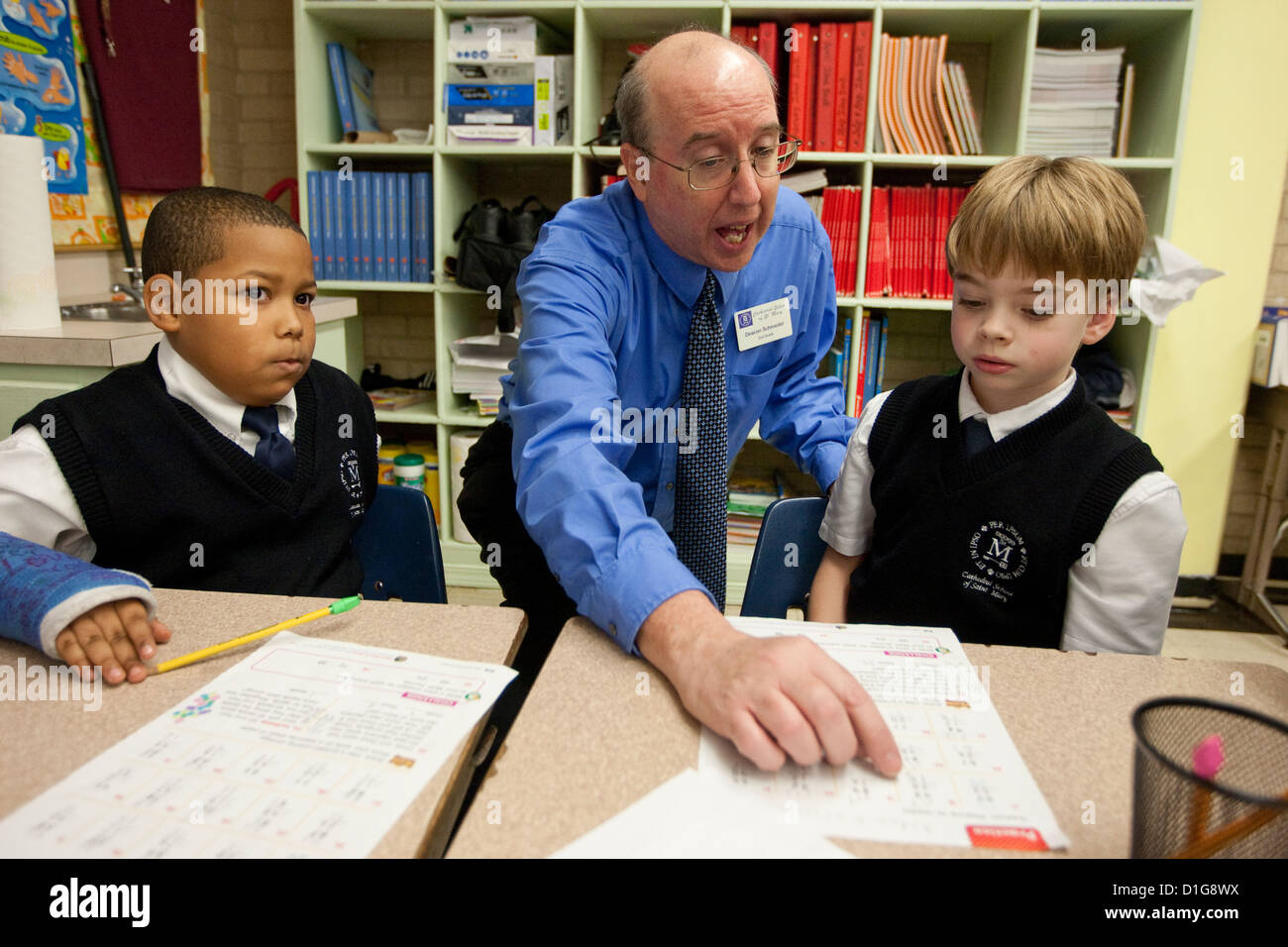 White male teacher assists African-American and Anglo students wearing uniform at private Catholic elementary school in Texas Stock Photo