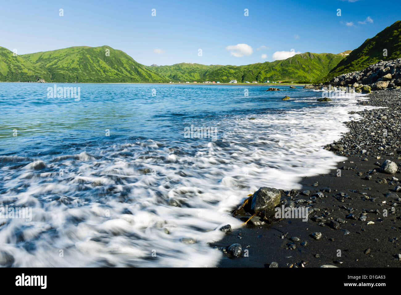Waves wash ashore at Pasagshak Bay with the village of Pasagshak in the background on Kodiak