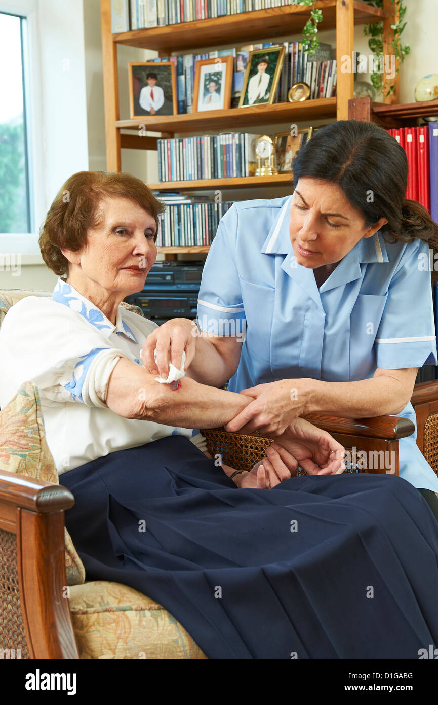 care worker wearing blue tunic attending to a wound on the arm of an elderly woman in her home Stock Photo