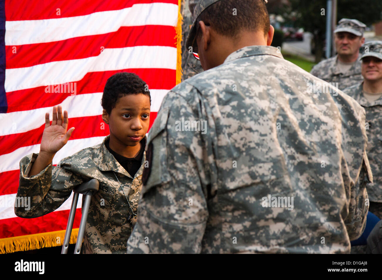 Khalil Quarles, 10, raises his right hand during his honorary enlistment into the Army Reserve as his father,  watches December 20, 2012 in Baltimore, MD. Khalil's dream is to be a soldier but suffers from a rare form of terminal cancer. Soldiers with the 200th Military Police Command showed up at Khalil's house and held a Enlistment Ceremony as well as providing a uniform, dogtags, a flag, and a ride in an armored Humvee. Stock Photo