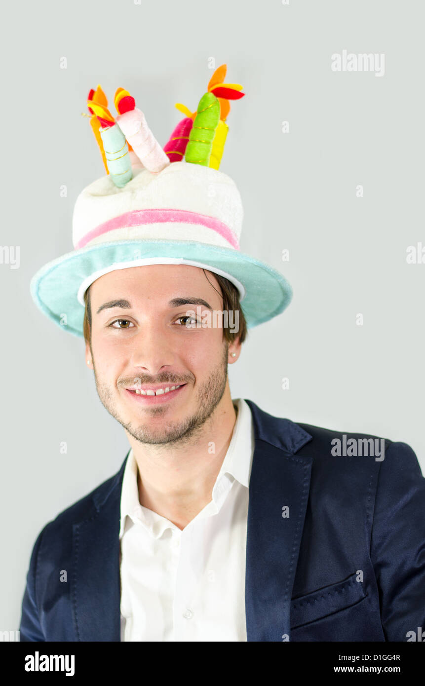 Cheerful, smiling, cute young man with funny birthday cake hat Stock Photo
