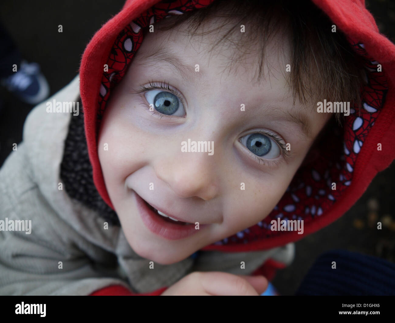 Small boy wearing a hooded jacket staring up at the camera with wide open eyes Stock Photo