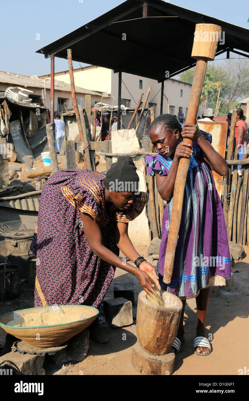 Two women pounding millet (sorgum) using mortar and pestel. Camp in a poor neigbourhood of Tsumeb, Namibia Stock Photo