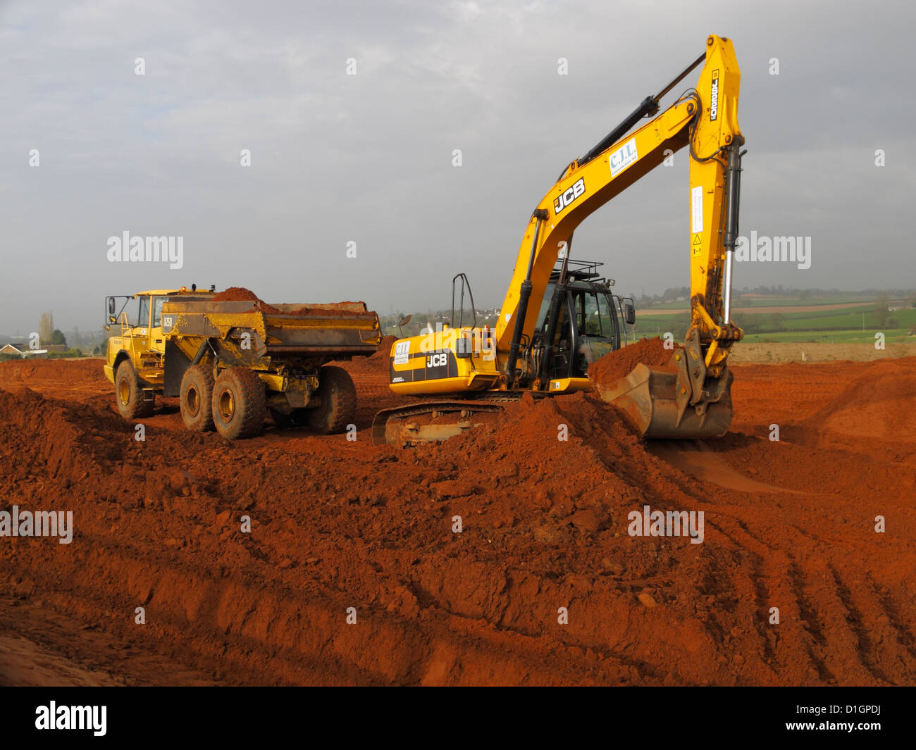 Tracked JCB backhoe excavator loading truck on highway construction building site UK Stock Photo