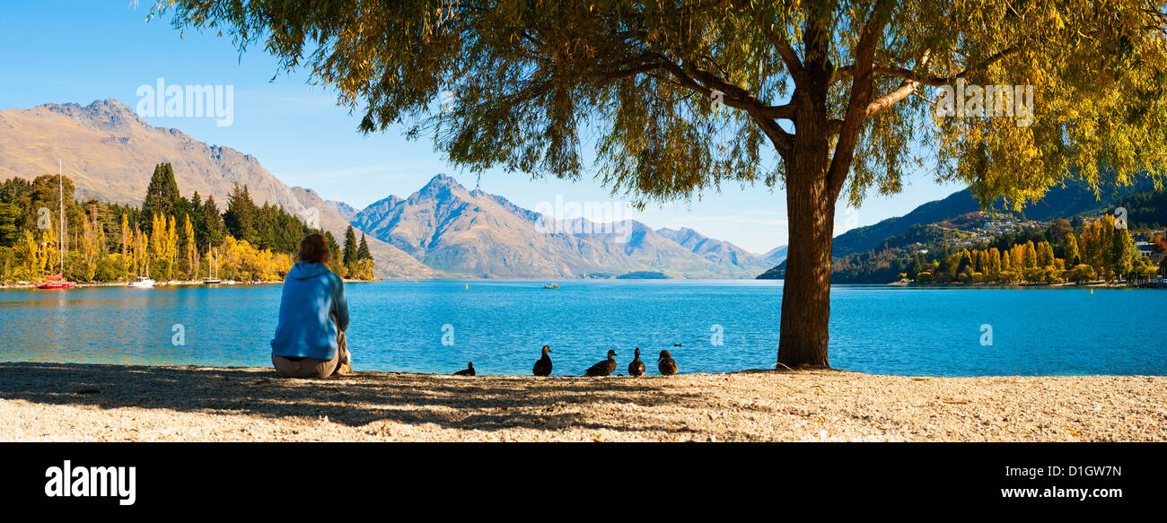 Panorama of a tourist relaxing by Lake Wakatipu in autumn at Queenstown, Otago, South Island, New Zealand, Pacific Stock Photo