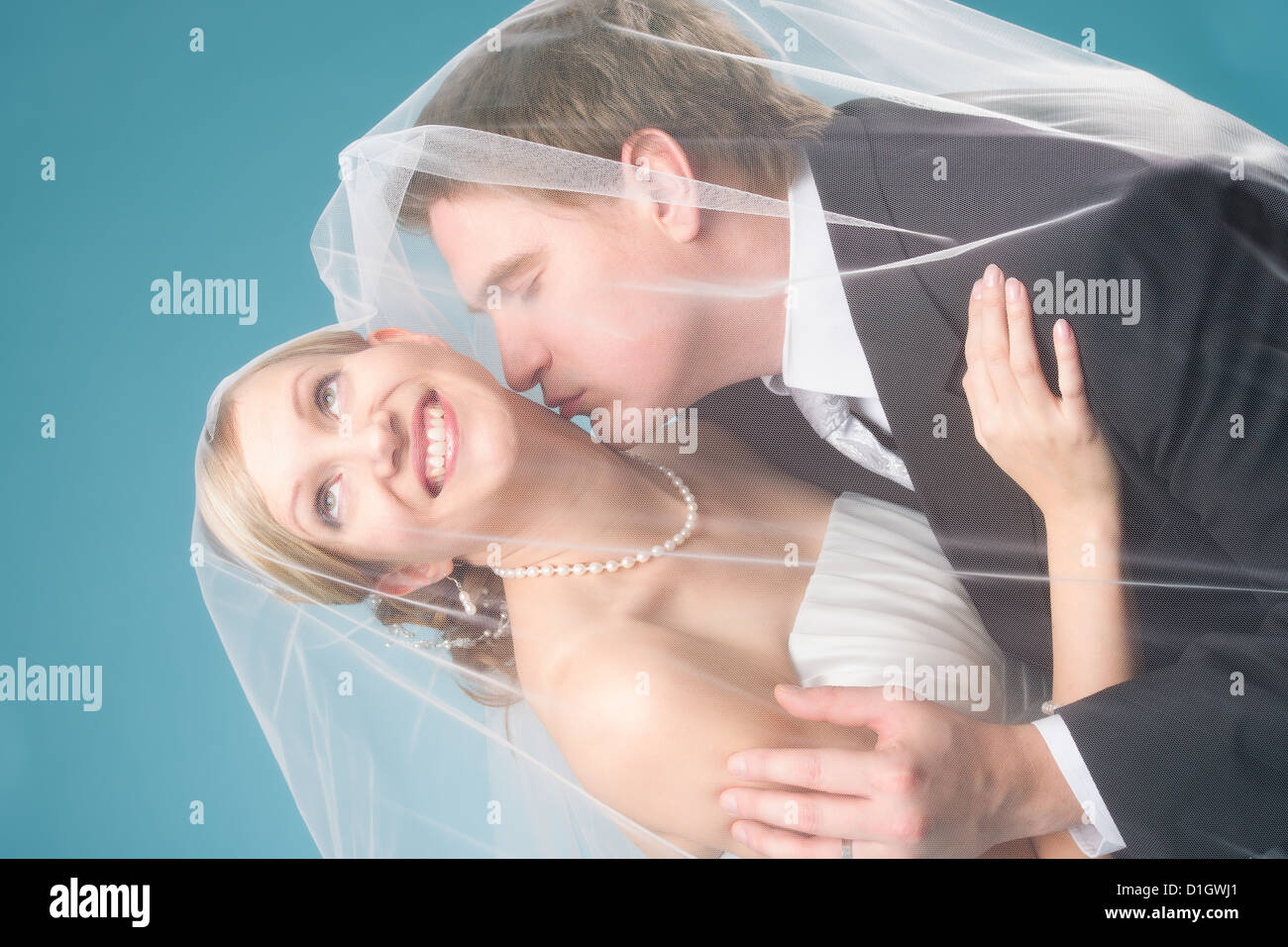 Groom give a kiss under a veil, happy bridal couple, blue background Stock Photo