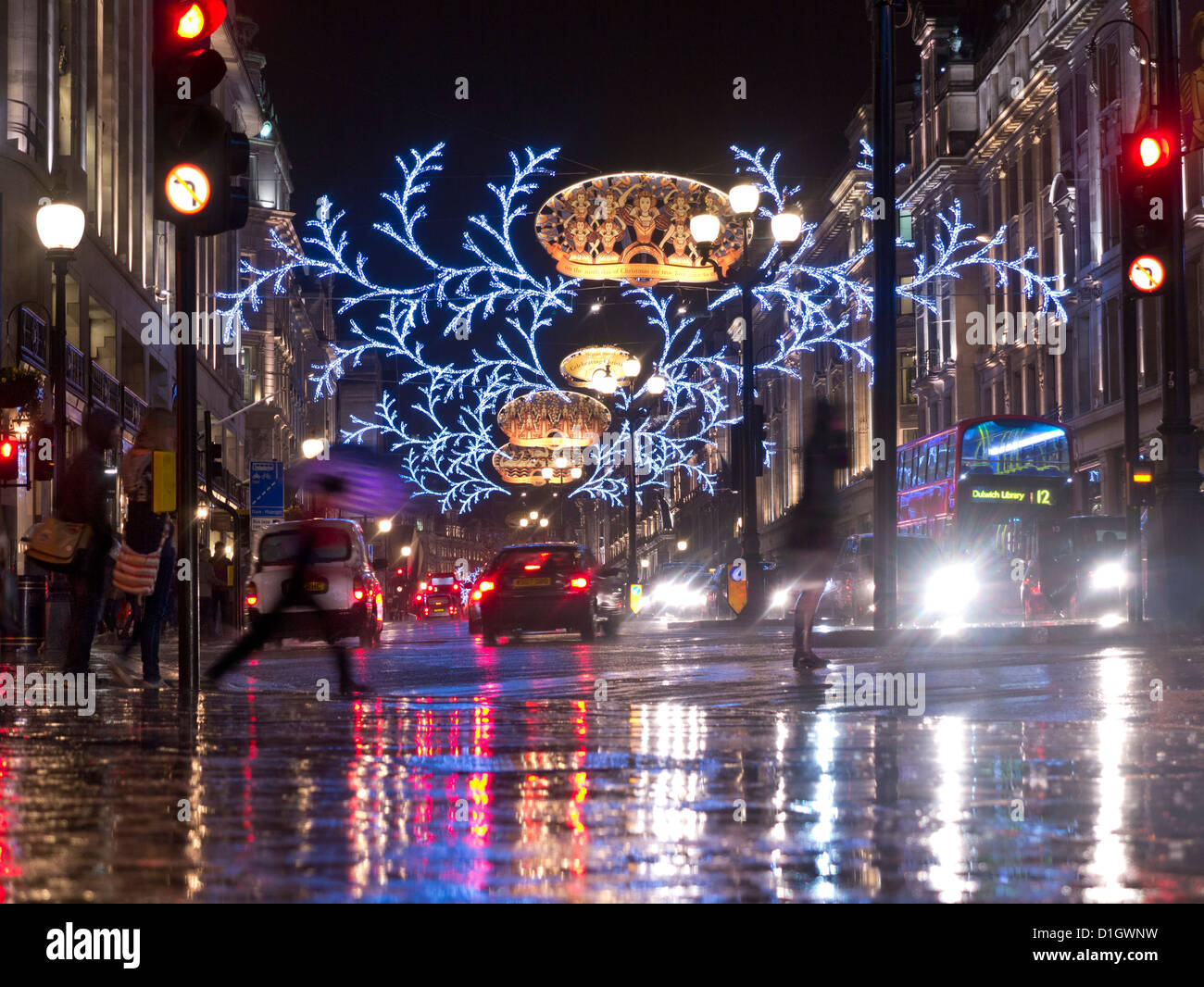 CHRISTMAS RAIN WET LIGHTS Busy scene of Christmas shoppers, traffic and umbrellas in a rain swept Regent Street with Christmas lights behind London UK Stock Photo