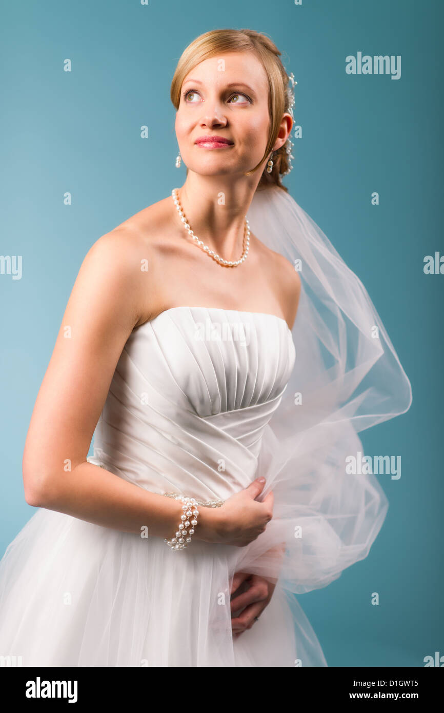 Beautiful bride wearing white wedding dress, blue background Stock Photo