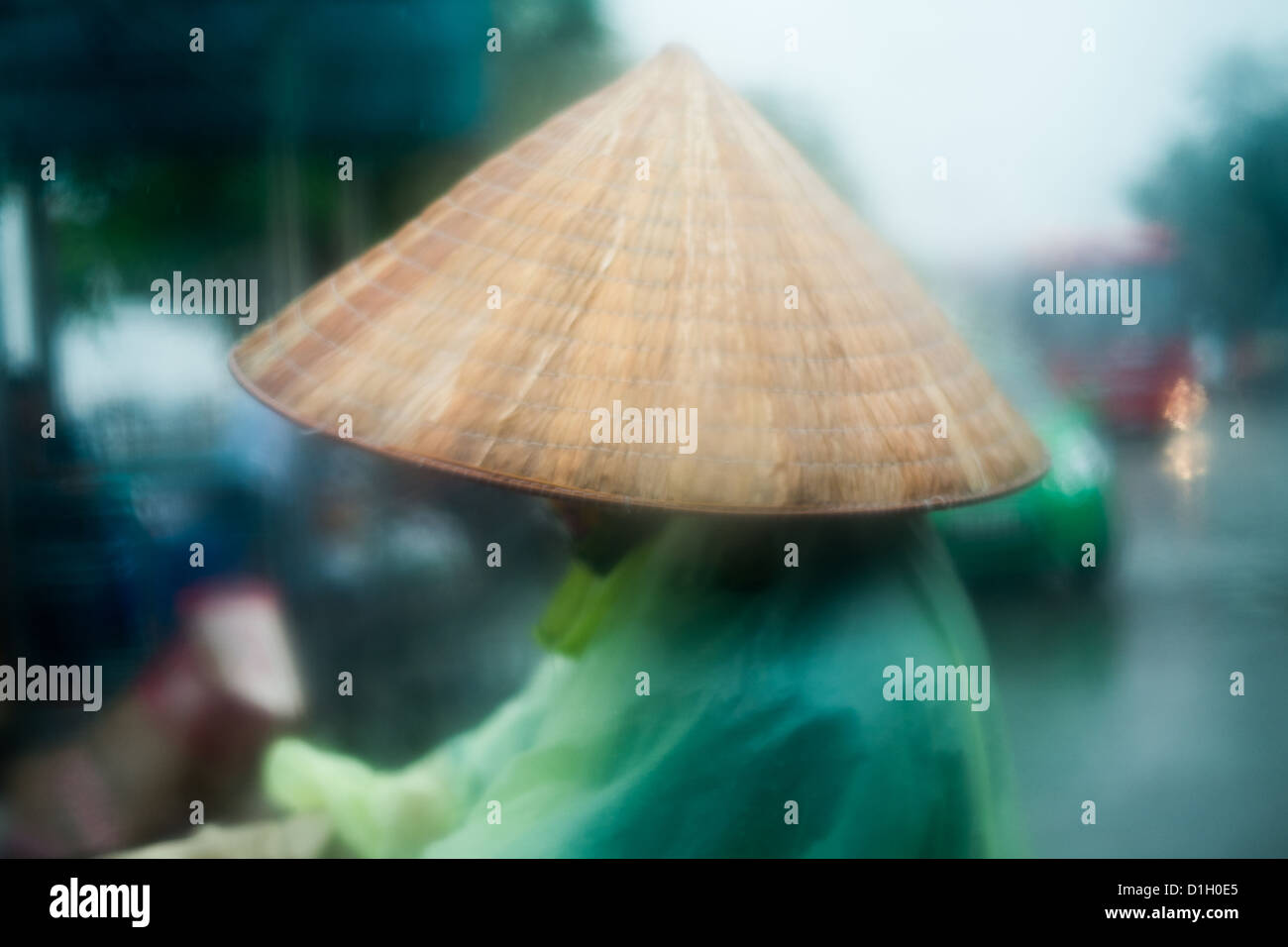 Vietnamese worker in bamboo hat and poncho working in a rain storm. Stock Photo