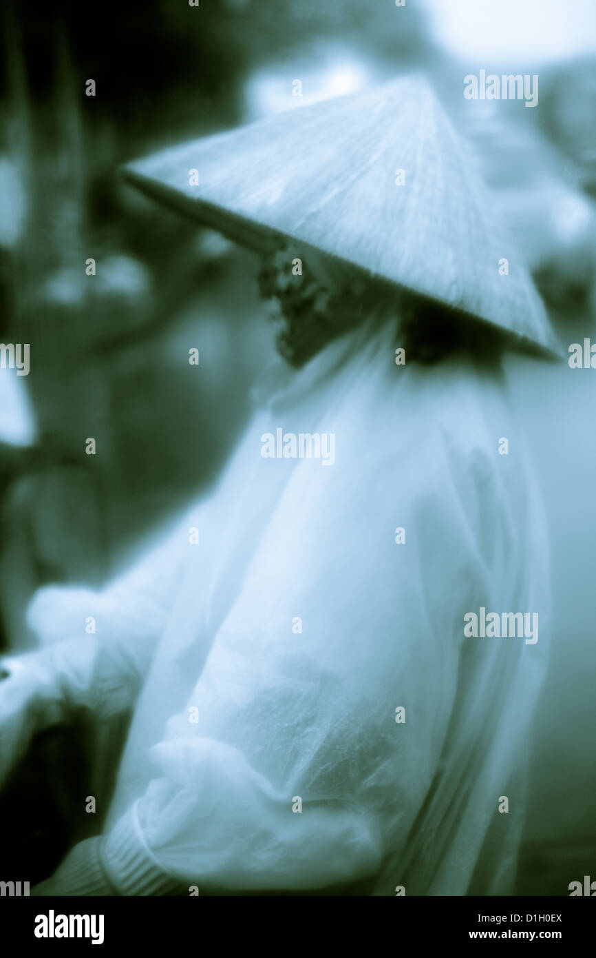 Vietnamese worker in bamboo hat and poncho working in a rain storm. Stock Photo