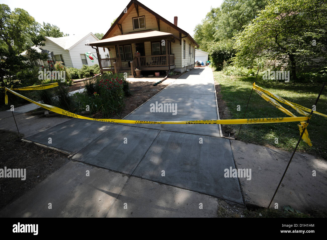 Yellow warning tape boundary around newly poured concrete driveway