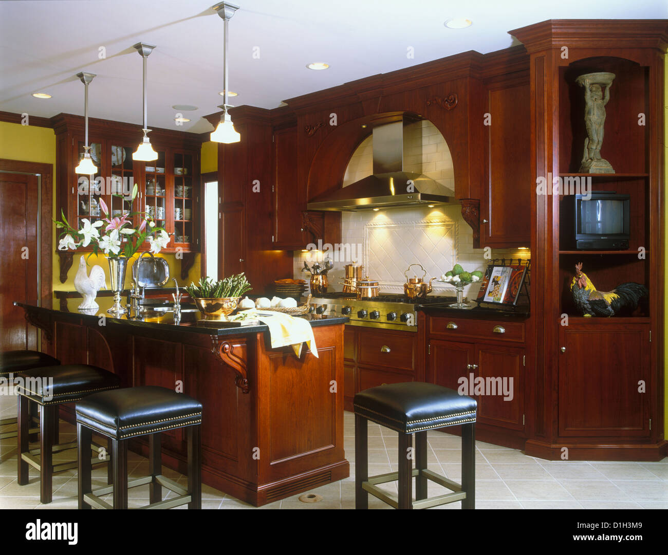 KITCHENS Cherry cabinets island with eating bar stools Countertops are black marble or granite Copper pots on stove ceramic Stock Photo