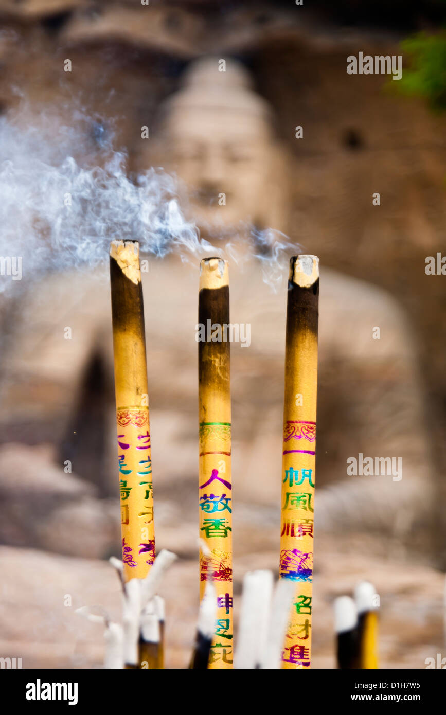 Three burning incense in front of a huge buddha statue. The focus is on