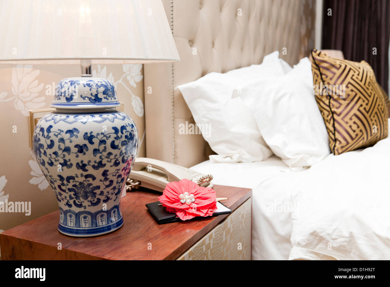 Ornate flower, note pad and telephone on the bed table in hotel room. Stock Photo